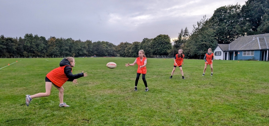 Four young players in orange bibs practising passes on a grass pitch at a Pentland Touch session