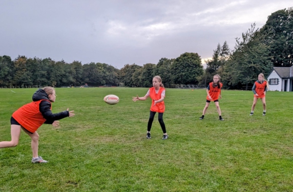Four young players in orange bibs practising passes on a grass pitch at a Pentland Touch session